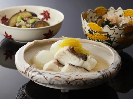 Drei Schalen mit japanischem Essen. Eine Schale enthält Fisch in Brühe, was ist dashi. Eine weitere Schale mit Auberginen und Edamame.