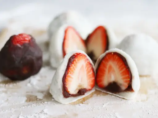 Erdbeeren-Wagashi-Rezept: Süße Mochi-Bällchen mit frischen Erdbeeren und roter Bohnenpaste, bestäubt mit Puderzucker.