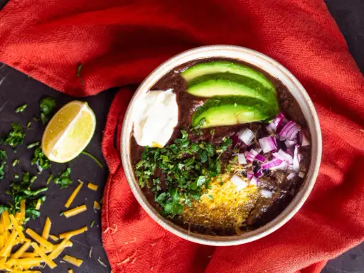 Herzhafter schwarze bohnen eintopf mit Avocado, Sauerrahm, Zwiebeln und Koriander. Ein Genuss für kalte Tage.