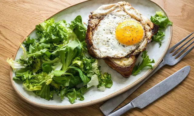 Ein Croque Madame mit Spiegelei, Käse und Toast, serviert mit frischem Salat.
