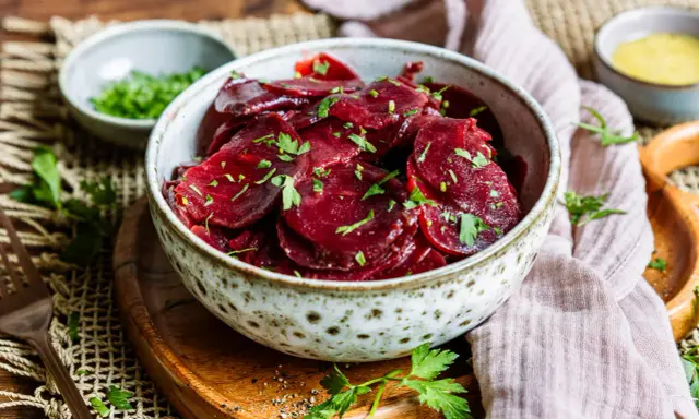Schüssel mit traditionellem Rote Bete Salat, garniert mit Petersilie. Daneben kleine Schälchen mit Kräutern und Dressing.