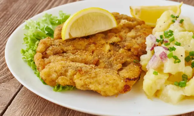Ein knuspriges Wiener Schnitzel mit Zitrone, Salat und Kartoffelsalat auf einem weißen Teller.