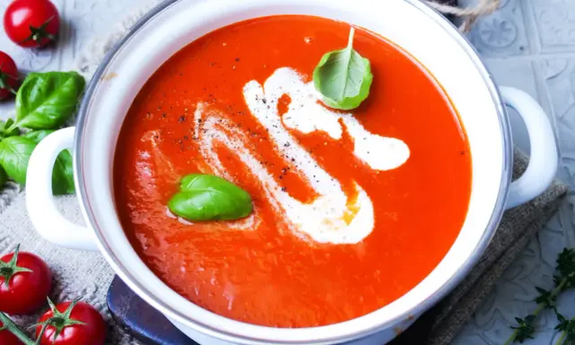 Eine cremige, beste Tomatensuppe mit Basilikum und einem Swirl Sahne, garniert mit frischen Tomaten und Kräutern.