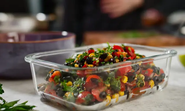 Frischer schwarze bohnen salat mit Mais, Tomaten und Kräutern in einer Glasbox, bereit zum Mitnehmen.