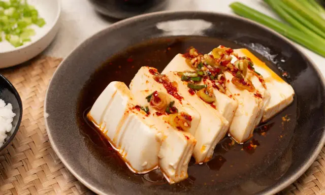 Seidiger Tofu, ein einfaches silken tofu recipe, serviert mit Frühlingszwiebeln und Chili-Öl auf einem dunklen Teller.