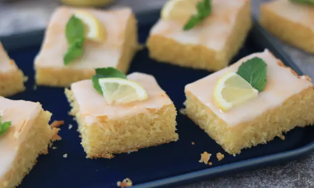Saftige Kuchenstücke mit Zitronenguss, garniert mit Zitronenspalten und Minze. Ein Genuss, der nach dem besten zitronenkuchen der welt schmeckt.