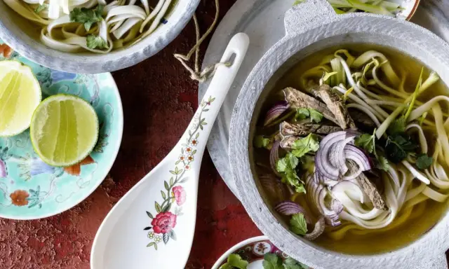 Ein dampfendes Pho-Rezept mit zarten Rindfleischscheiben, Reisnudeln, Sojasprossen und frischem Koriander in einer aromatischen Brühe. Dazu Limettenspalten.