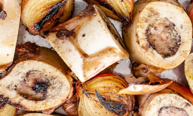 Rinderknochen auskochen Rezept: Geröstete Rinderknochen und Zwiebeln auf einem Blech, bereit für eine herzhafte Brühe.