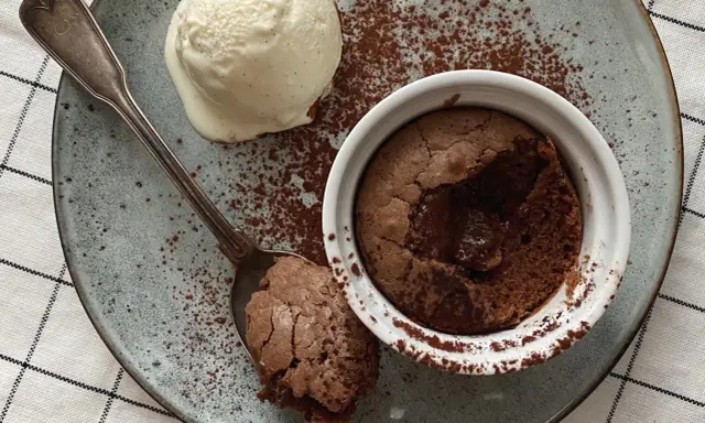 Ein warmer, flüssiger Kern im Moelleux au chocolat, serviert mit einer Kugel Vanilleeis und Kakaopulver.