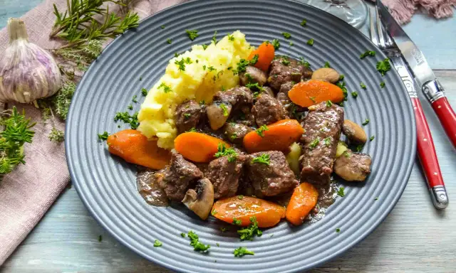 Herzhaftes Boeuf Bourguignon Rezept mit zartem Rindfleisch, Karotten, Pilzen und Kartoffelpüree, garniert mit Petersilie.