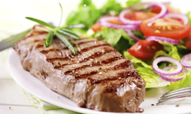 Ein saftiges Steak mit Grillstreifen, garniert mit Rosmarin, neben einem frischen Salat aus knackigem Grün, Tomaten und roten Zwiebelringen. Ein perfekter Steak Salat.