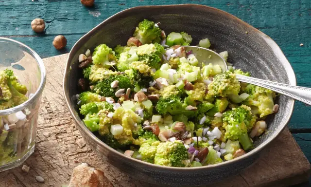 Ein einfacher Brokkoli-Salat mit Nüssen und Rosinen, serviert in einer Schüssel auf einem Holztisch.
