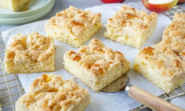 Saftige Stücke vom besten Apfelkuchen mit Streusel, frisch gebacken und bereit zum Genießen. Äpfel liegen daneben.