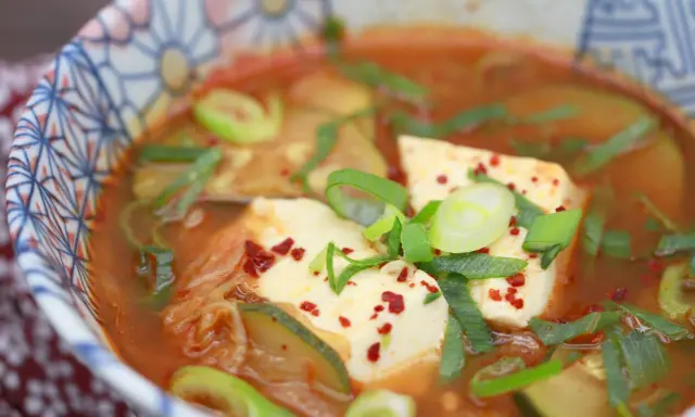 Heißes, würziges Sundubu Jjigae mit weichem Tofu, Kimchi und Frühlingszwiebeln in einer bunten Schüssel.