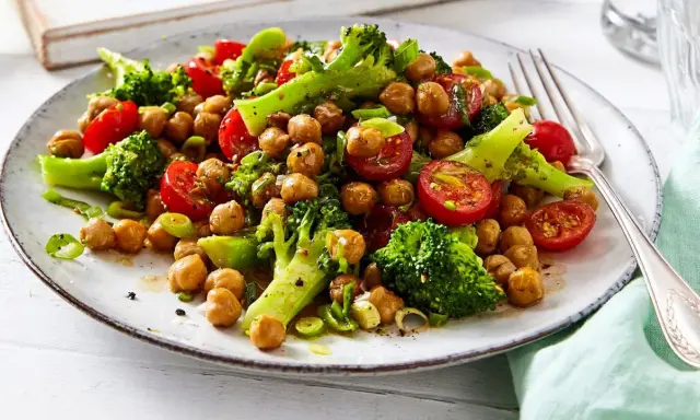 Frischer brokkoli kichererbsen salat mit Kirschtomaten und Frühlingszwiebeln auf einem Teller, appetitlich angerichtet.