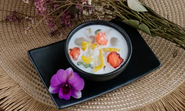 Schüssel mit cremigen asiatischen Nachspeisen, garniert mit Früchten und einer Orchidee.