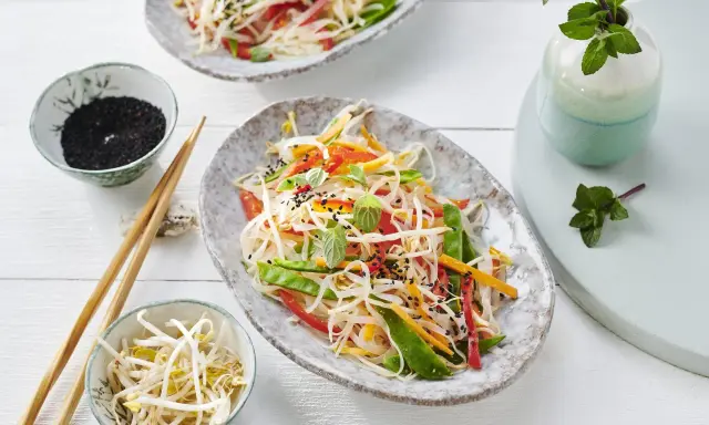 Frischer Glasnudelsalat mit knackigem Gemüse, garniert mit Sesam und Minze. Daneben Schüsselchen mit Sprossen und schwarzem Sesam.