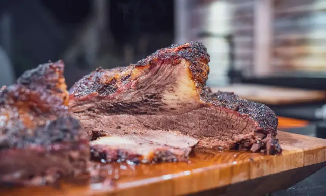 Saftiges Rind Brisket mit dunkler Kruste, auf einem Holzbrett serviert. Der Rauch steigt auf und verspricht ein zartes Geschmackserlebnis.