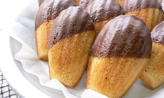 Eine Reihe von Madeleines, die zur Hälfte in Schokolade getaucht sind, warten darauf, gegessen zu werden.