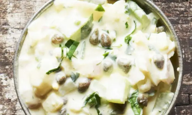 Cremiger Kartoffelsalat mit Kapern und frischen Kräutern, serviert in einer Metallschale auf rustikalem Holz.
