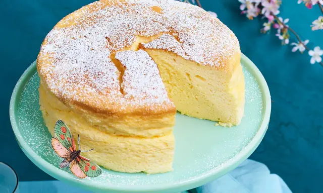 Ein luftiger, japanischer Kuchen, bestäubt mit Puderzucker, steht auf einem mintgrünen Tortenständer. Ein Schmetterling sitzt am Rand.