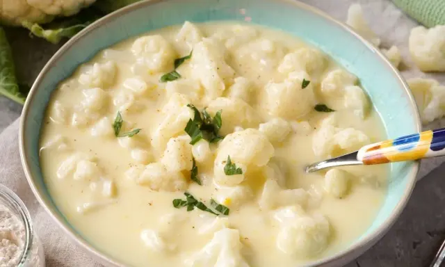 Cremige blumenkohlsuppe thermomix ohne kartoffeln, garniert mit Petersilie. Ein Löffel mit buntem Muster liegt in der Schüssel.