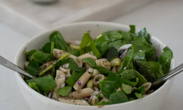 Ein frischer nudelsalat mit spargel, garniert mit Spinat und roten Zwiebeln, bereit zum Genießen.