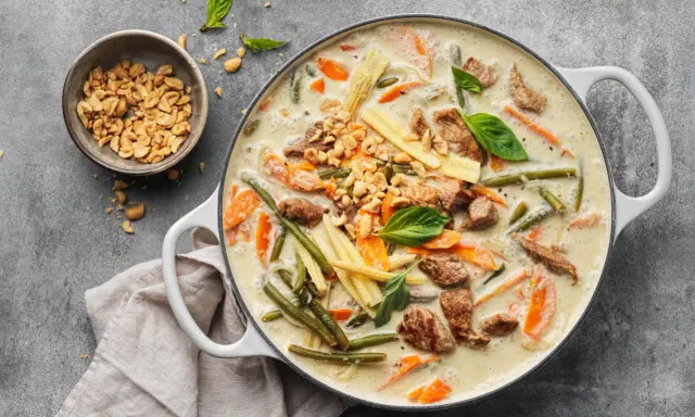 Herzhaftes Thai Curry mit Rindfleisch, zarten Möhren, grünen Bohnen und Maiskolben in cremiger Kokosmilch, garniert mit Erdnüssen und Basilikum.