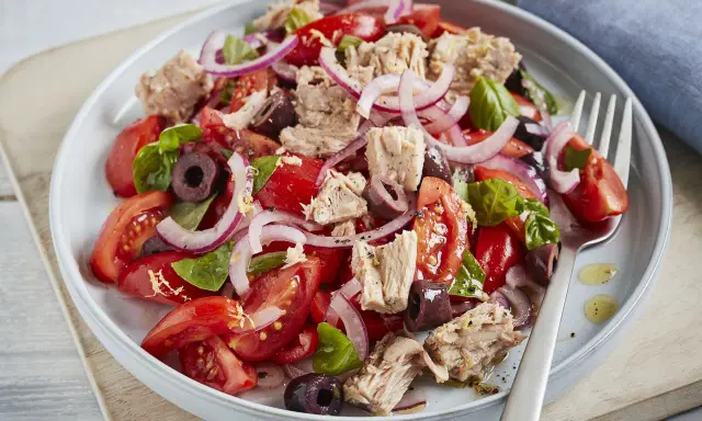 Frischer Tomaten-Thunfisch-Salat mit roten Zwiebeln und Oliven, garniert mit Basilikum. Ein leichter und gesunder Genuss.