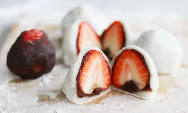 Erdbeeren-Wagashi-Rezept: Süße Mochi-Bällchen mit frischen Erdbeeren und roter Bohnenpaste, bestäubt mit Puderzucker.