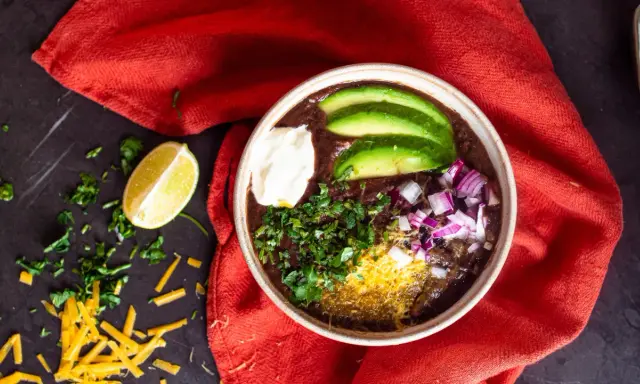 Herzhafter schwarze bohnen eintopf mit Avocado, Sauerrahm, Zwiebeln und Koriander. Ein Genuss für kalte Tage.