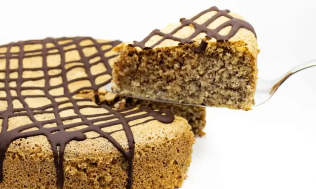 Ein Stück zuckerfreier Kuchen mit Schokoladenglasur wird aus einem Ganzen gehoben.