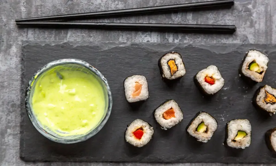 Sushi mit Lachs, Avocado und Paprika, dazu eine grüne Soße. Ist Wasabi gesund? Ja, es ist bekannt für seine entzündungshemmenden Eigenschaften.