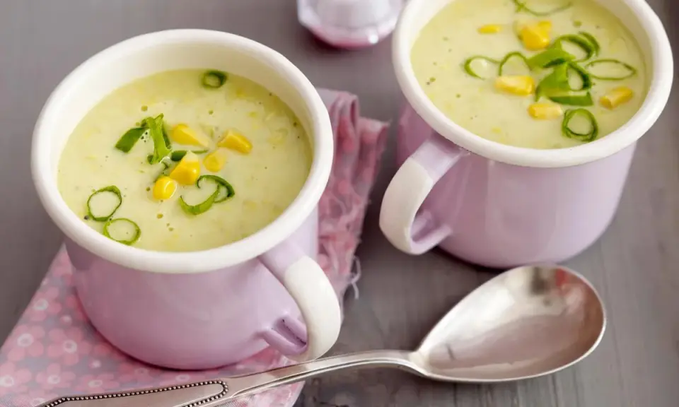 Zwei Tassen cremiger Maissuppe mit Kokosmilch, garniert mit Maiskörnern und Frühlingszwiebeln.