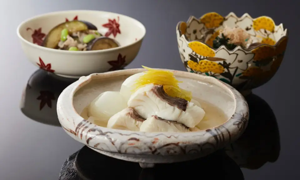 Drei Schalen mit japanischem Essen. Eine Schale enthält Fisch in Brühe, was ist dashi. Eine weitere Schale mit Auberginen und Edamame.