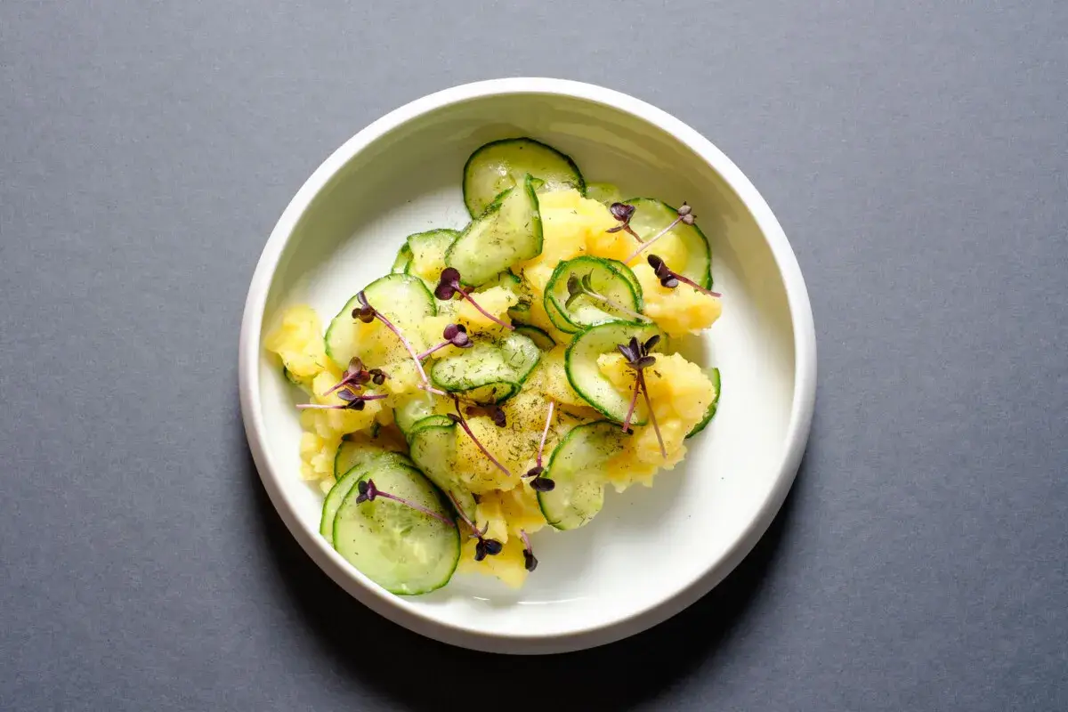 Kartoffelsalat mit frischer Gurke, garniert mit lila Sprossen und Dill. Ein leichter und erfrischender Genuss.