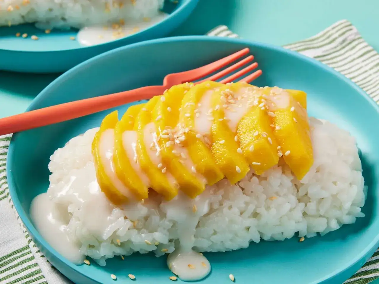Ein Teller mit Mango Sticky Rice, garniert mit Sesam. Süßer Klebreis mit Kokosmilch und frischen Mangoscheiben.