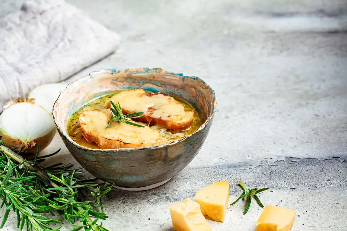 Herzhaftes Zwiebelsuppe Rezept Original: goldbraun überbackene Brotscheiben mit Käse auf aromatischer Zwiebelsuppe, garniert mit Rosmarin.