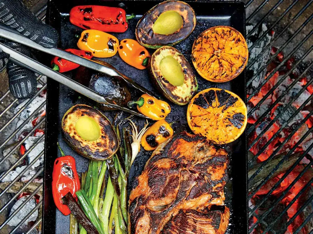 Fleisch, Avocado, Orangen und Gem&uuml;se werden auf einer Plancha &uuml;ber gl&uuml;hender Kohle gegrillt.