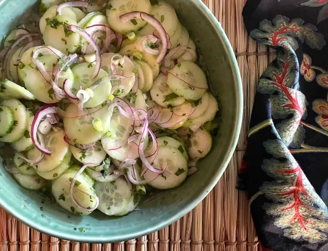 Frischer gurkensalat asiatisch mit roten Zwiebeln und Kr&auml;utern in einer gr&uuml;nen Sch&uuml;ssel.