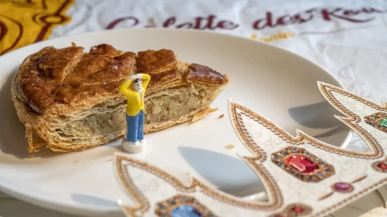 Ein Stück Galette des Rois mit einer kleinen Figur und Krönchen. Die Galette des Rois Tradition ist ein Fest für die ganze Familie.