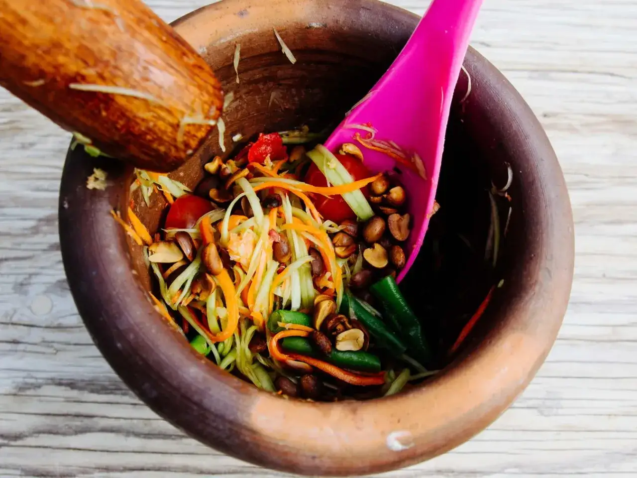 Frischer Thai Salat mit Papaya, Karotten, Bohnen und Erdnüssen wird in einem Mörser zubereitet.