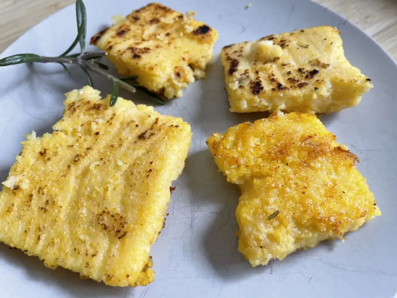Gebratene Polenta-Quadrate auf einem Teller, garniert mit Rosmarin. Was ist Polenta? Ein herzhaftes Gericht aus Maisgrieß.