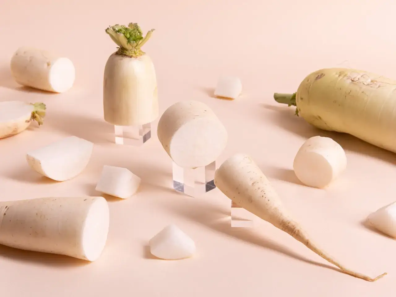 Mehrere daikon rettich St&uuml;cke, einige ganz, andere geschnitten, liegen auf einem hellen Untergrund.