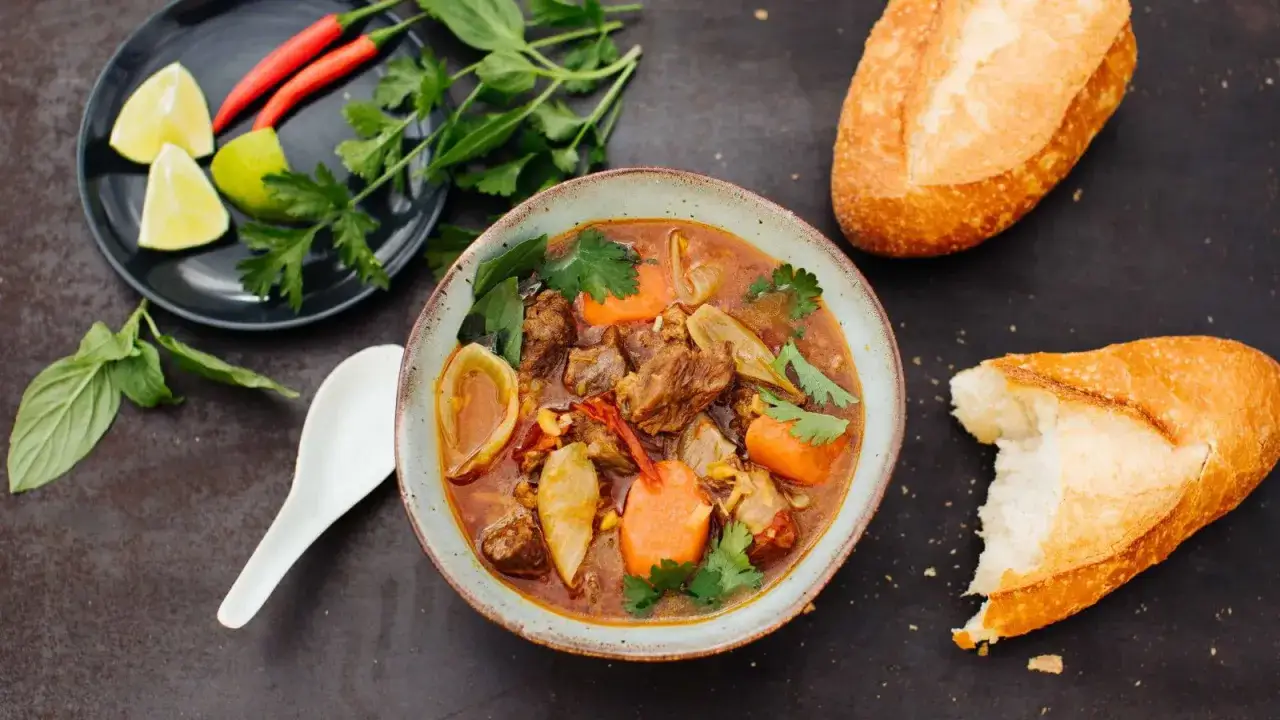 Herzhaftes Bo Kho, ein vietnamesischer Rindfleischeintopf mit Karotten und Kräutern, serviert mit Baguette.