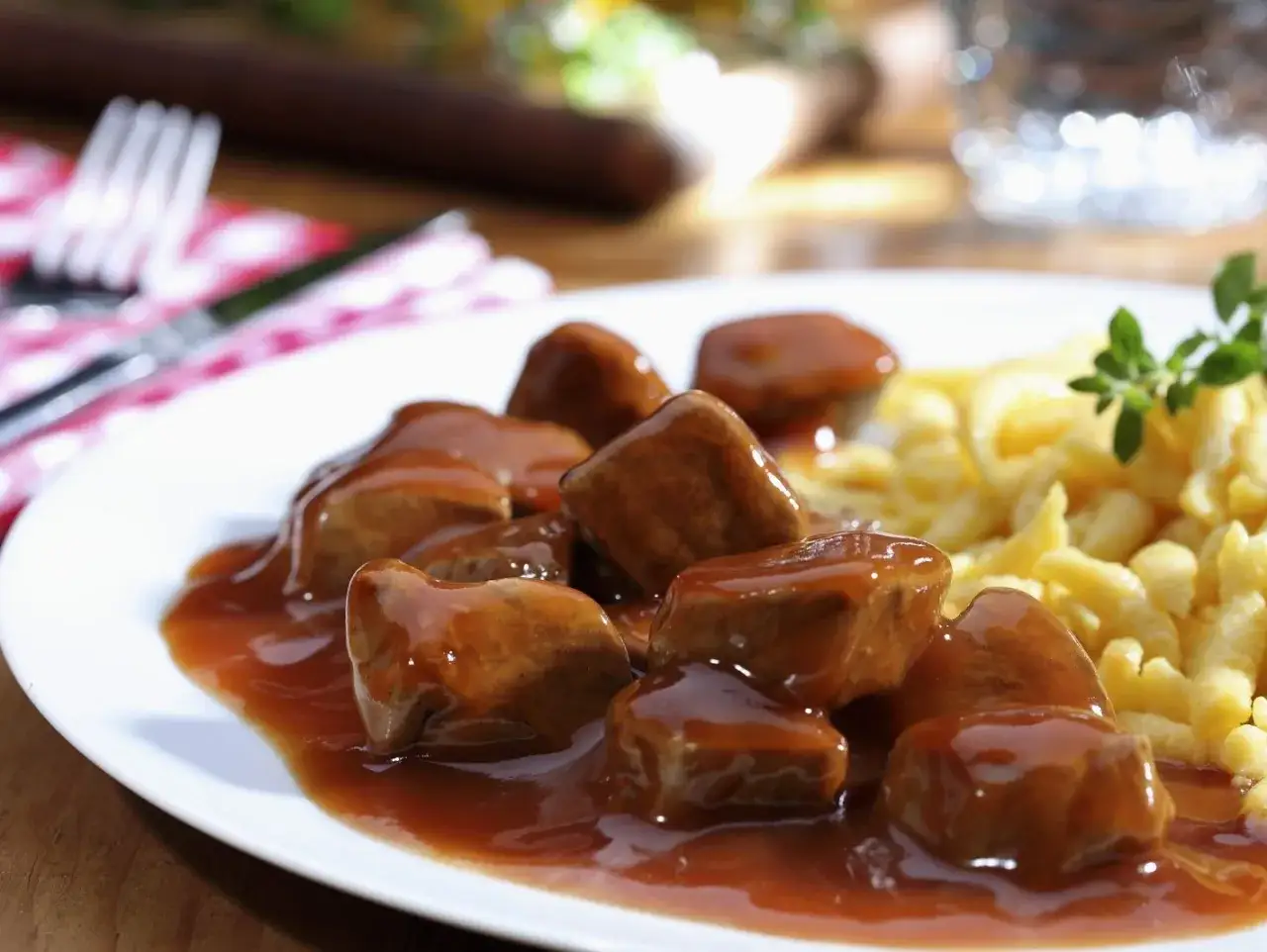 Ein Teller mit saftigen Kalbfleischwürfeln in dunkler Sauce und Spätzle. Ein Festmahl, das nach dem besten Kalbsgulasch schmeckt.