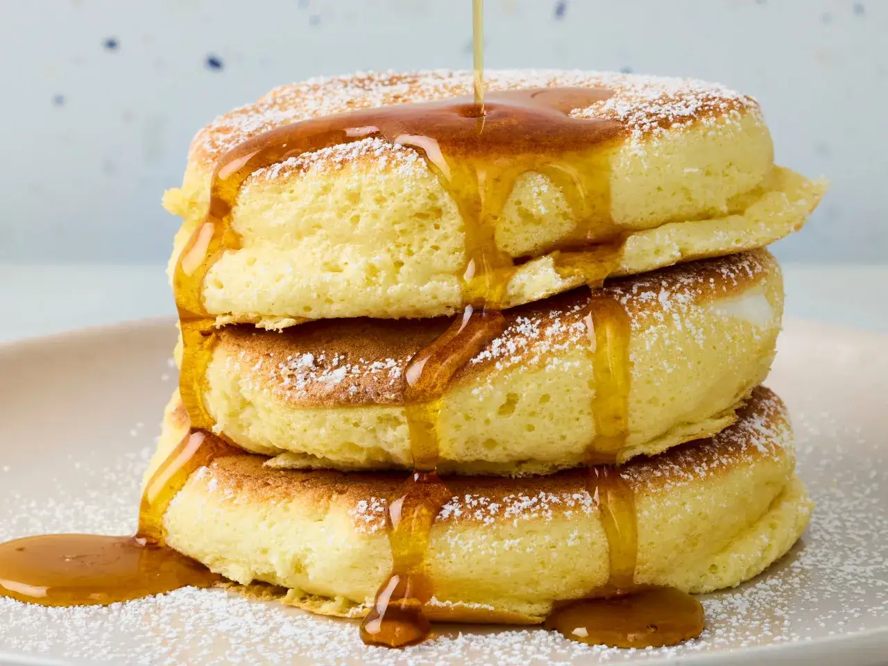 Fluffige japanische Pancakes, bestäubt mit Puderzucker und übergossen mit goldenem Sirup, ein süßer Genuss.