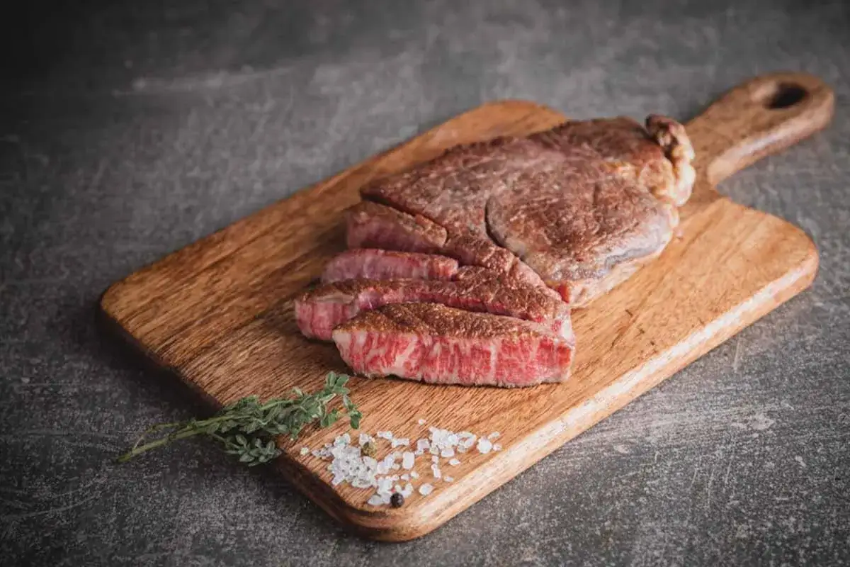 Ein saftiges Steak, das zeigt, was ist wagyu fleisch: zart, marmoriert und auf einem Holzbrett mit Kr&auml;utern und Salz angerichtet.