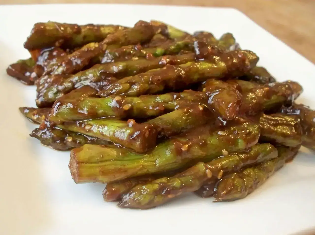 Ein Haufen glasiertes spargel asiatisch mit Sesam auf einem weißen Teller.