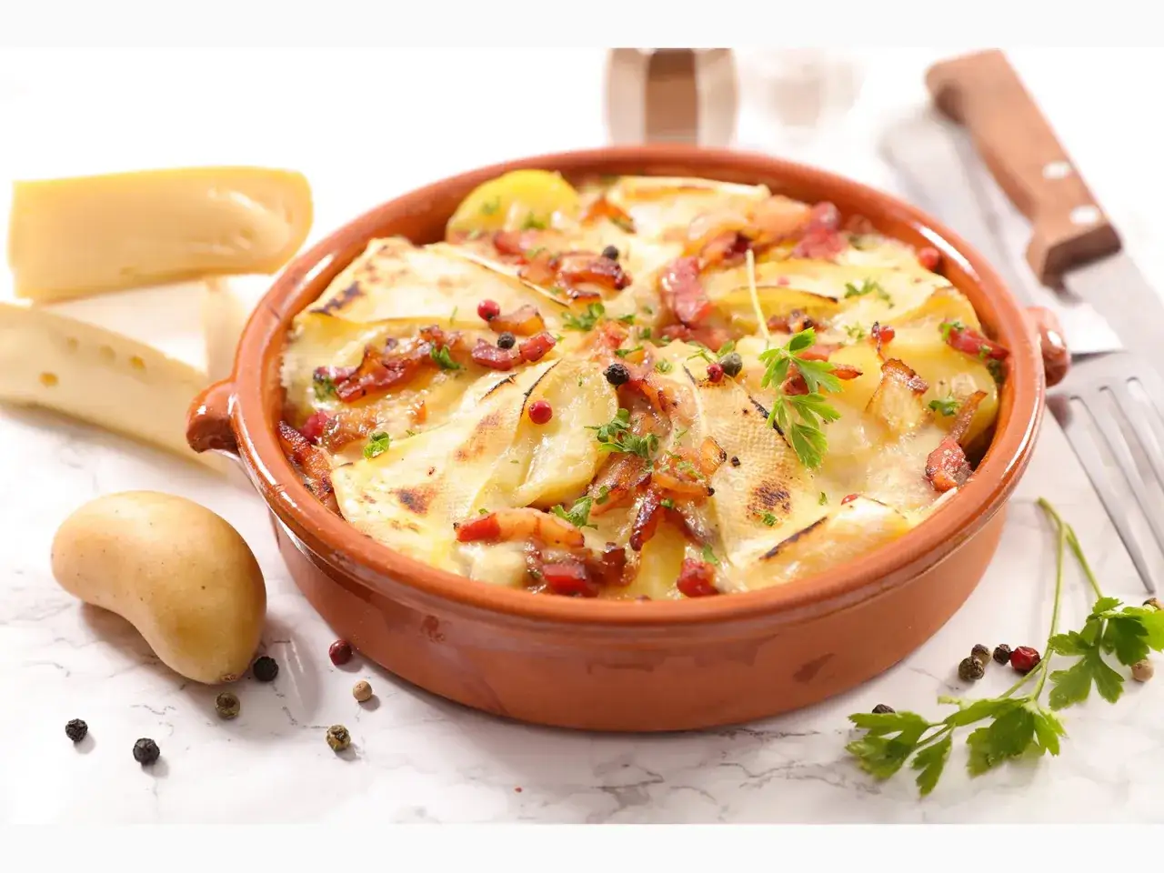 Herzhaftes Tartiflette-Rezept: Kartoffeln, Speck und Käse in einer Auflaufform, garniert mit Petersilie und Pfefferkörnern.